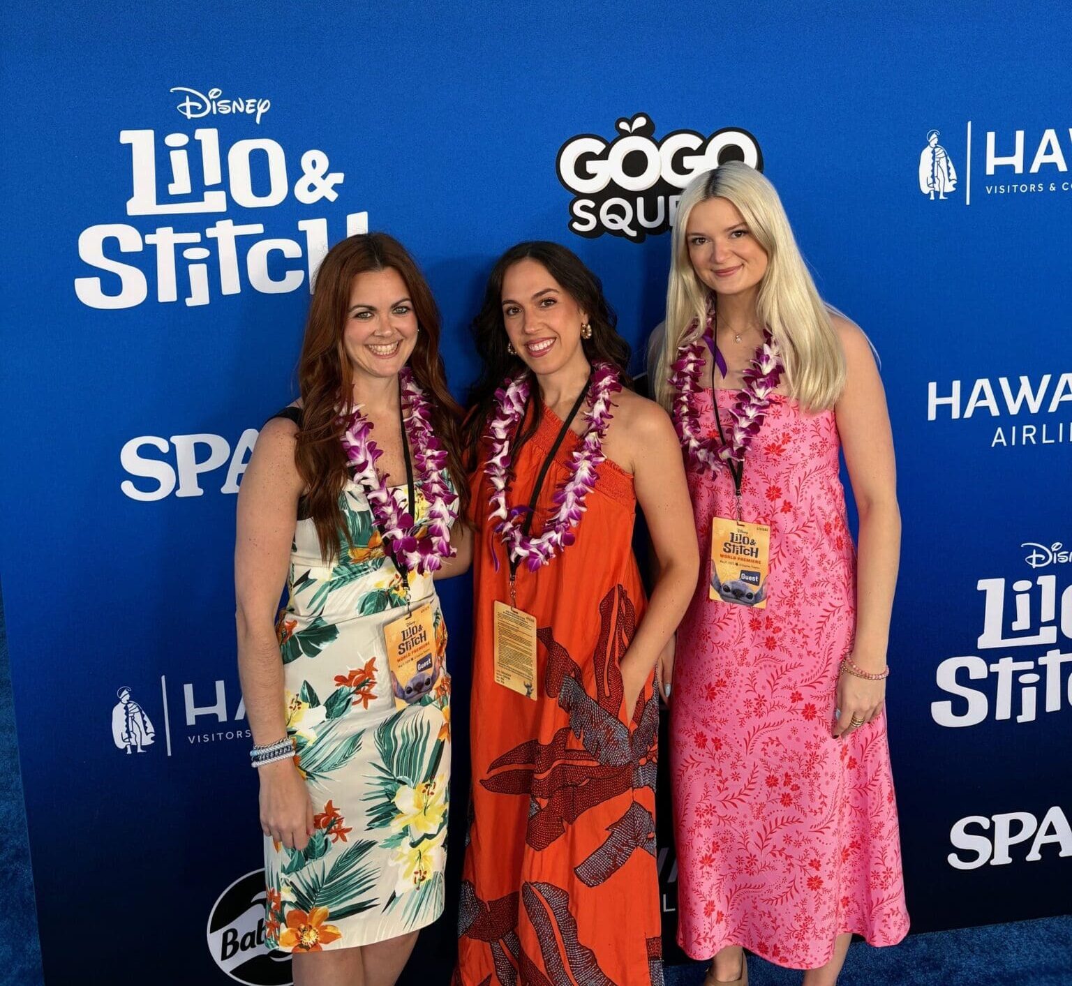 Three women at the Disney premiere for Lilo & Stitch with a GoGo squeeZ sponsored backdrop