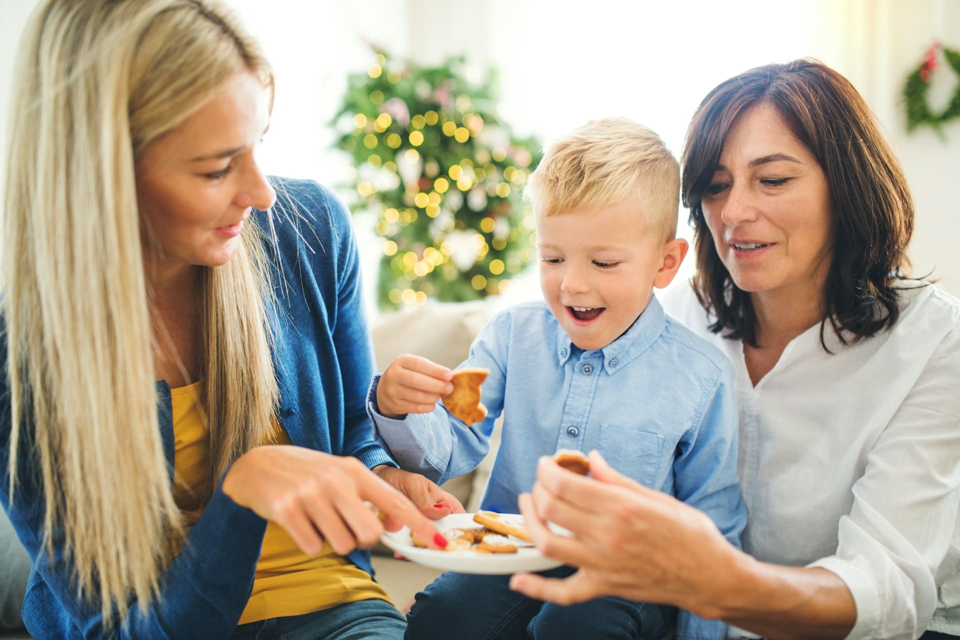 A child sitting between two adult women while holding holiday cookies in a winter holiday decorated setting.